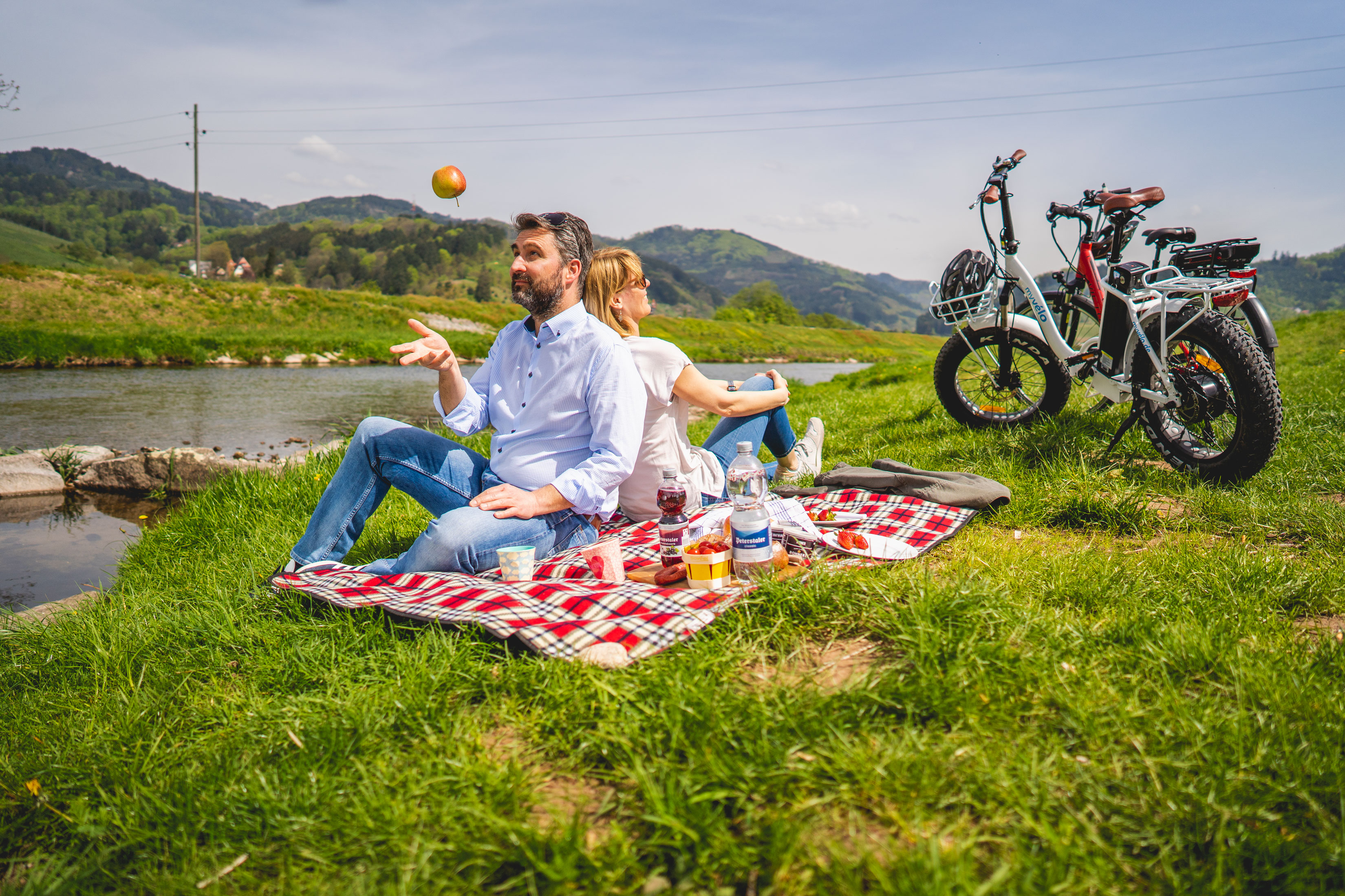 Ein Paar sitzt mit der Picknickdecke an der Rench, Fahrräder im Hintergrund
