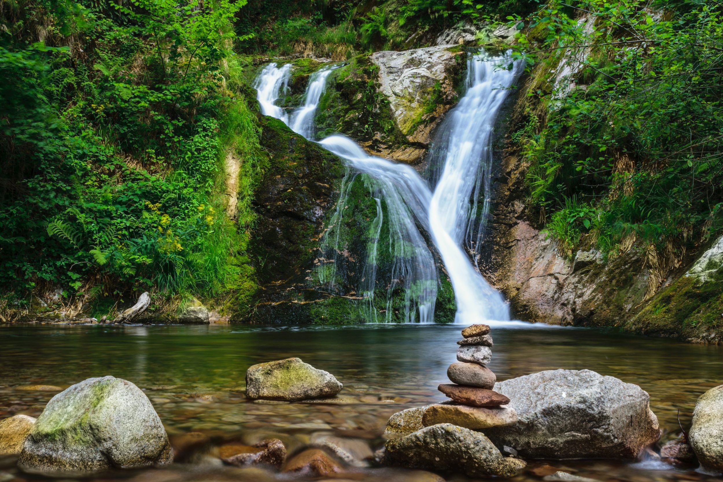 Wasserfälle aus zwei Richtungen enden in einem kleinen See, umgeben von Wald