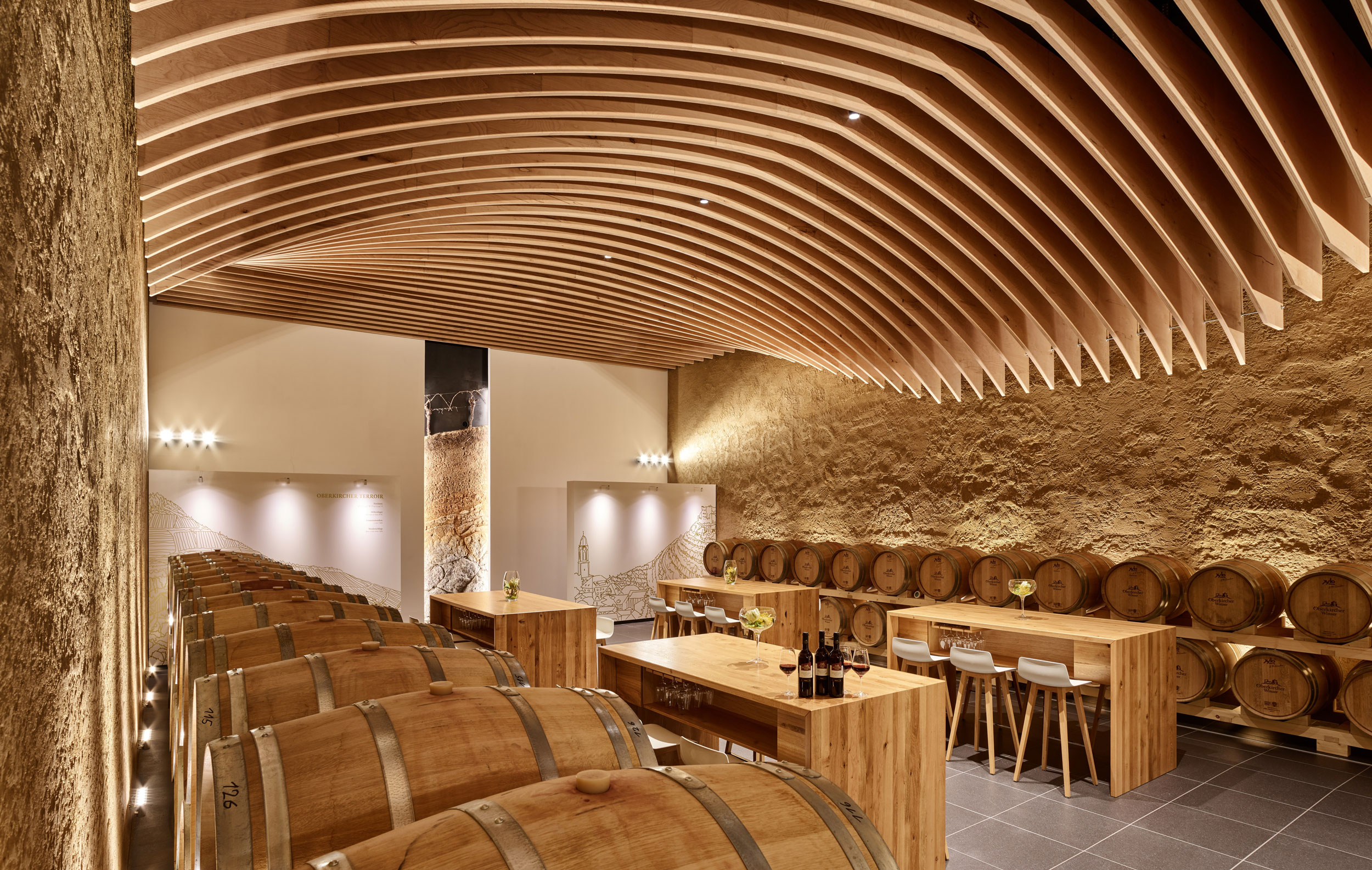 Das Bild zeigt das Oberkircher Vinotorium. Es gibt Sitzmöglichkeiten und große Holzfässer für Wein. Der Raum ist modern gestaltet