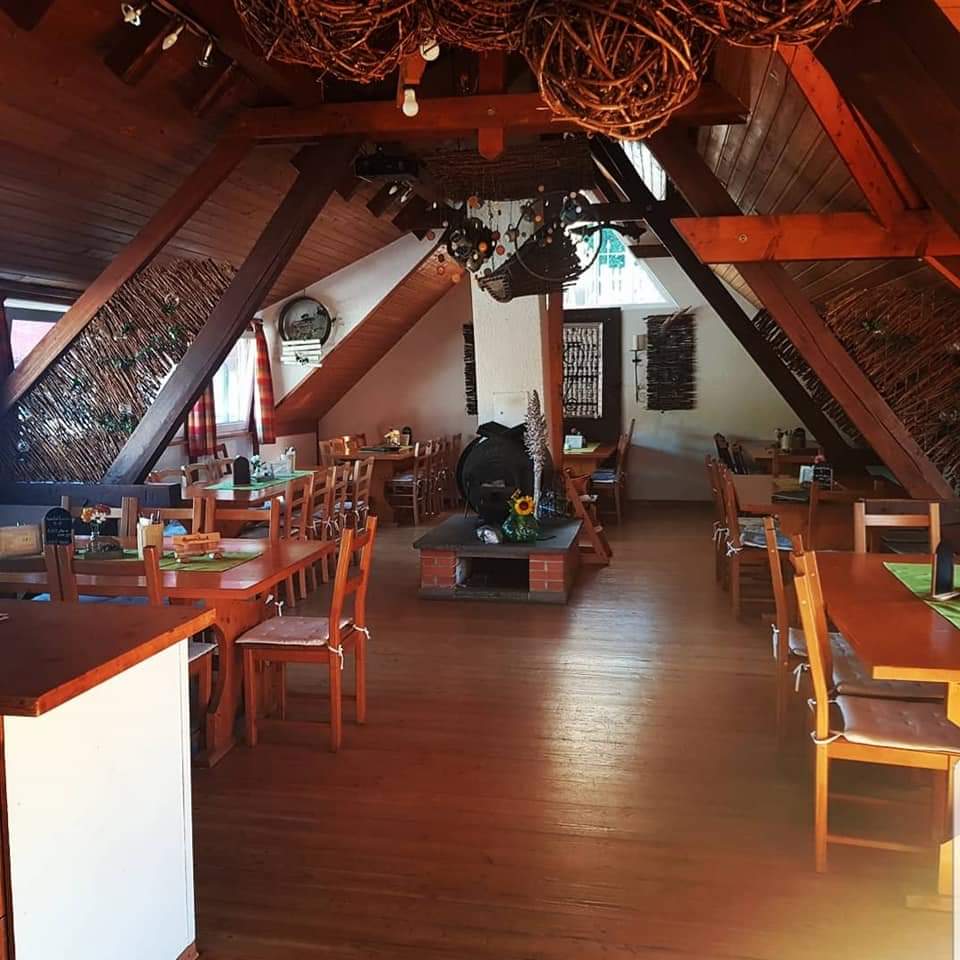 Ein Dachgeschossraum für Veranstaltungen. Tische mit Stühlen und eine Theke sind zu sehen. 